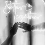 Black and white photo of couple's hands reaching towards each other with 'Better Together' neon sign.